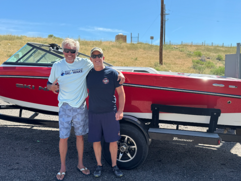 2022 Ski Nautique 200 Two people smiling in front of a red boat on a trailer in sunny weather.